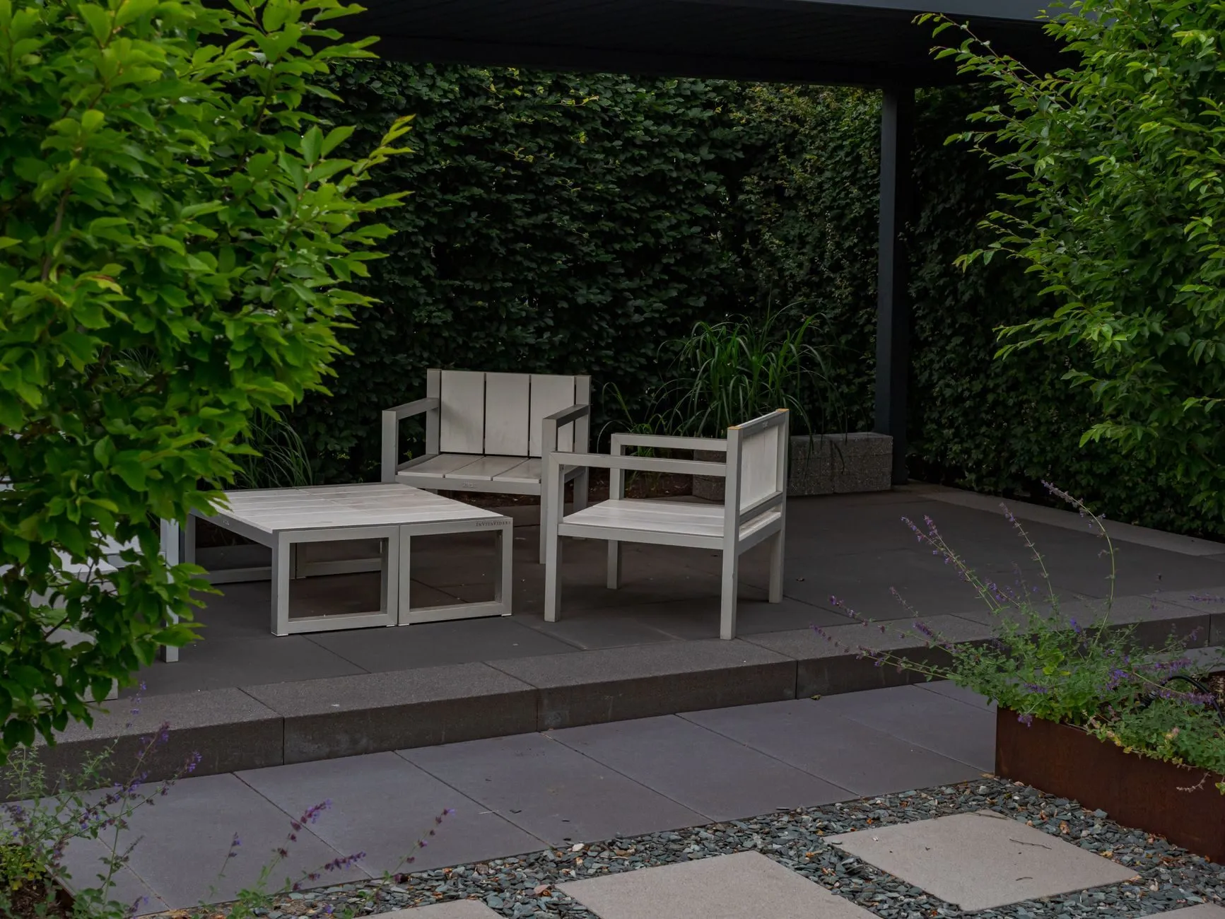 A covered porcelain terrace with white timber chairs, stepping stones in gravel